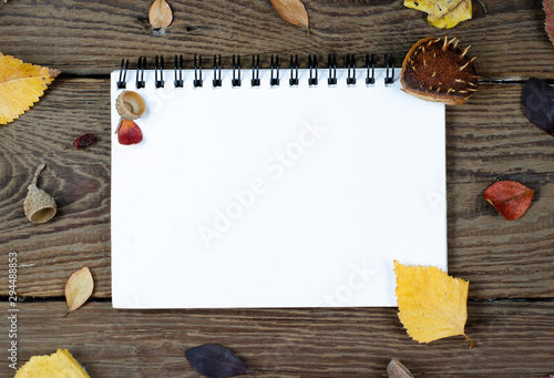Autumn composition on wooden  background . Blank notepad covered with autumn rust leaves, chestnuts, acorns . Top view , copy space  flat lay.