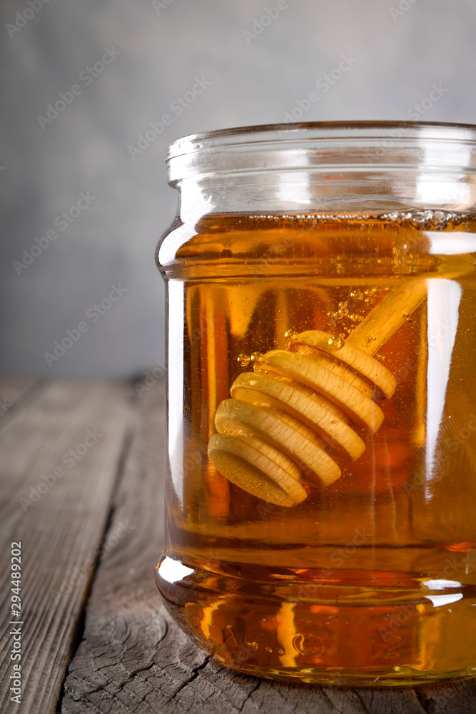 Pouring aromatic honey into jar, closeup. Honey in glass jars and honeycombs wax on wooden background. Wooden stick , instruments Pouring aromatic honey into jar, closeup. Honey in glass jars and honeycombs wax on wooden background. Wooden stick , instruments