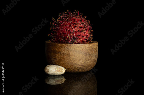 Group of one whole one piece of fresh red rambutan in wooden bowl isolated on black glass