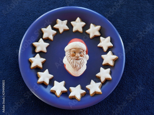 Christmas plate with the face of Santa Claus . Blue ceramic plate, decorated with home-baked cinnamon stars, isolated against a blue background. photo