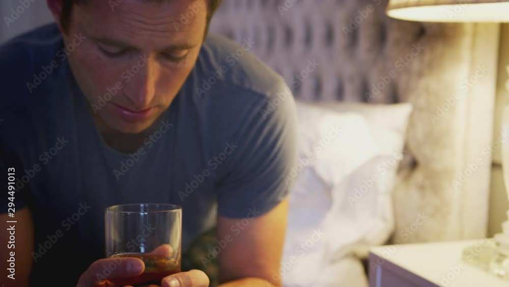 Depressed Man Wearing Pajamas Sitting On Side Of Bed With Glass Of Whisky On Bedside Cabinet Depressed Man Wearing Pajamas Sitting On Side Of Bed With Glass Of Whisky On Bedside Cabinet