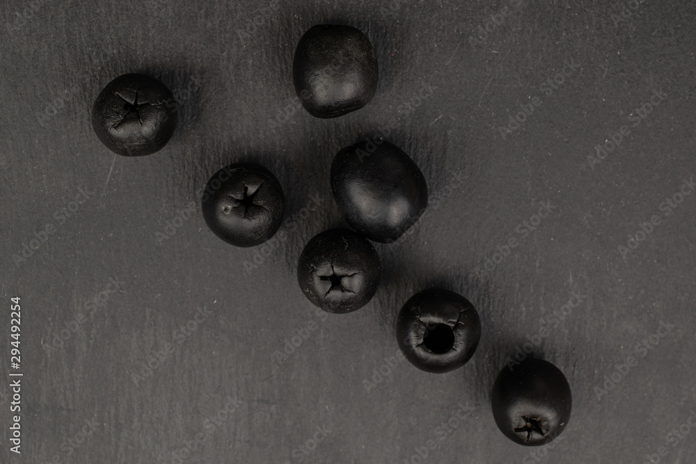 Group of seven whole tasty black olive flatlay on grey stone Group of seven whole tasty black olive flatlay on grey stone