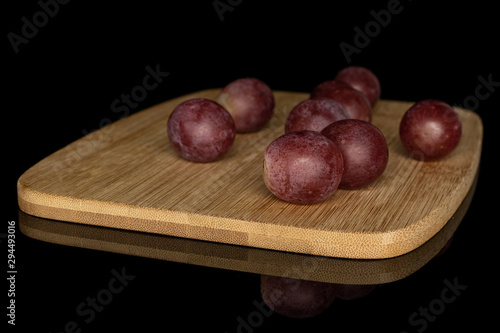 Lot of whole disordered fresh purple grape rose on bamboo cutting board isolated on black glass