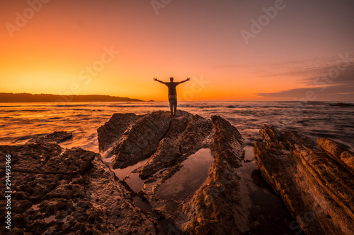 Hendaye, Aquitaine / France »; October 7, 2019: A young man on top of some rocks on a sunset in Hendaye