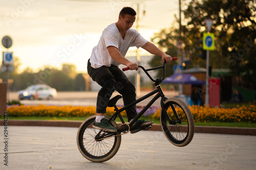 The guy performs a BMX stunt while standing on the rear wheel.