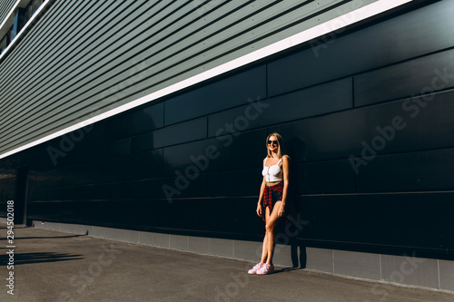 girl in summer clothes and sunglasses posing in the street against a black wall