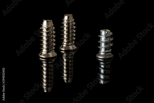 Group of three whole metallic glossy bolt isolated on black glass