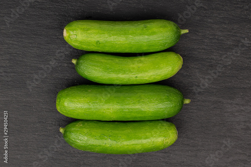 Group of four whole mini green cucumber in row flatlay on grey stone