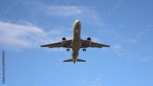 Modern passenger plane flies overhead, exactly in the center of the frame. In the background there is a beautiful blue sky and white clouds. The airplane is landing, taking off. Ultra HD stock footage
