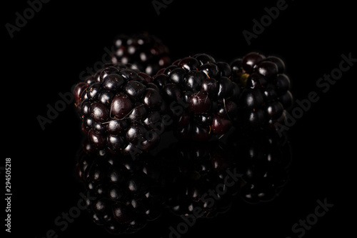 Group of four whole fresh black blackberry isolated on black glass