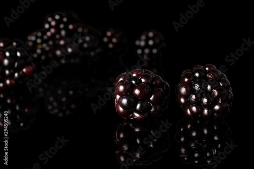 Lot of whole fresh black blackberry two in focus isolated on black glass photo