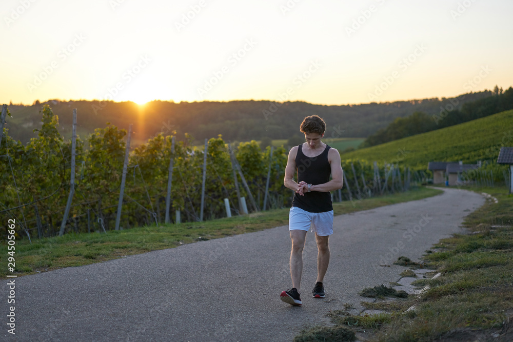 relaxed young runner looking at his watch in sunset