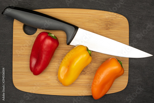 Group of three whole fresh pepper on bamboo cutting board with steel knife flatlay on grey stone photo