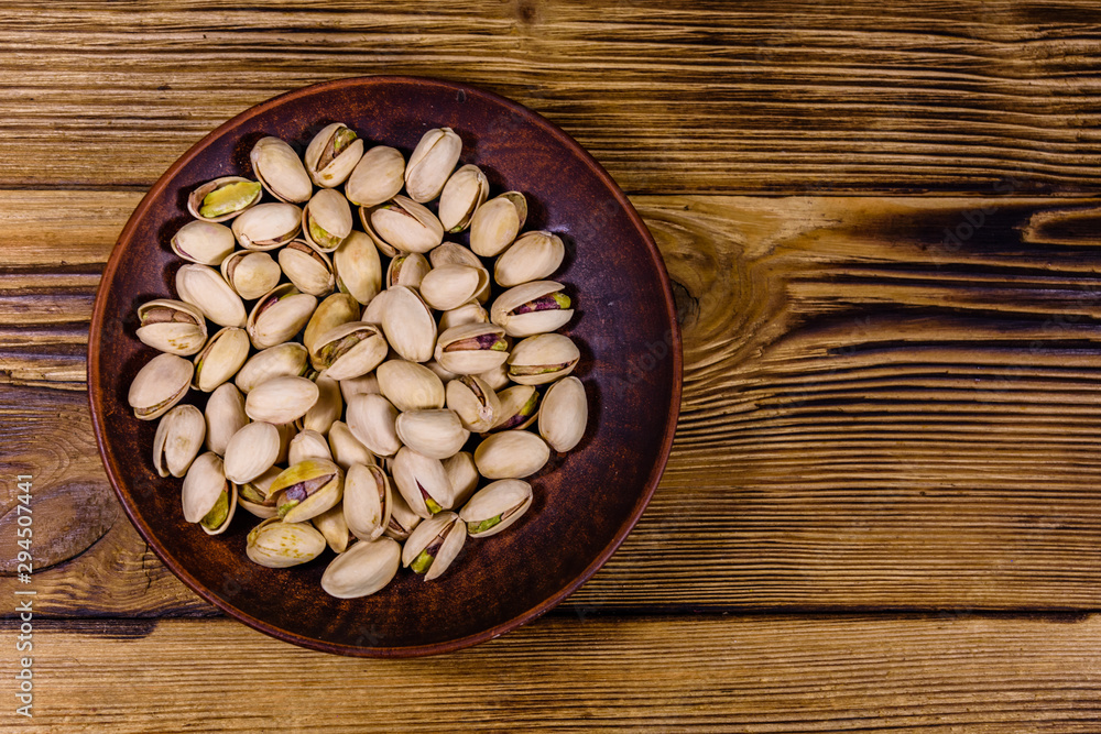 Ceramic plate with pistachio nuts on a wooden table. Top view Ceramic plate with pistachio nuts on a wooden table. Top view