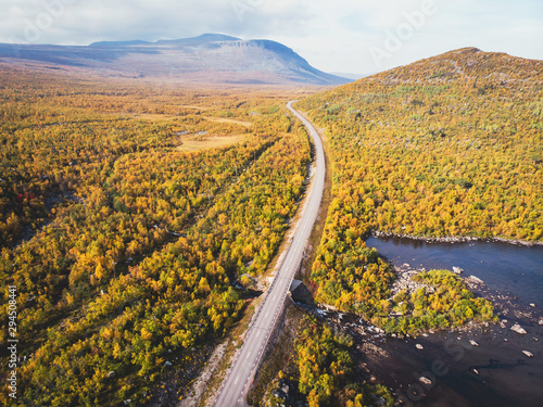 Aerial sunny fall autumn view of Abisko National Park, Kiruna Municipality, Lapland, Norrbotten County, Sweden, shot from drone, with Abiskojokk river, road and Nuolja mountain