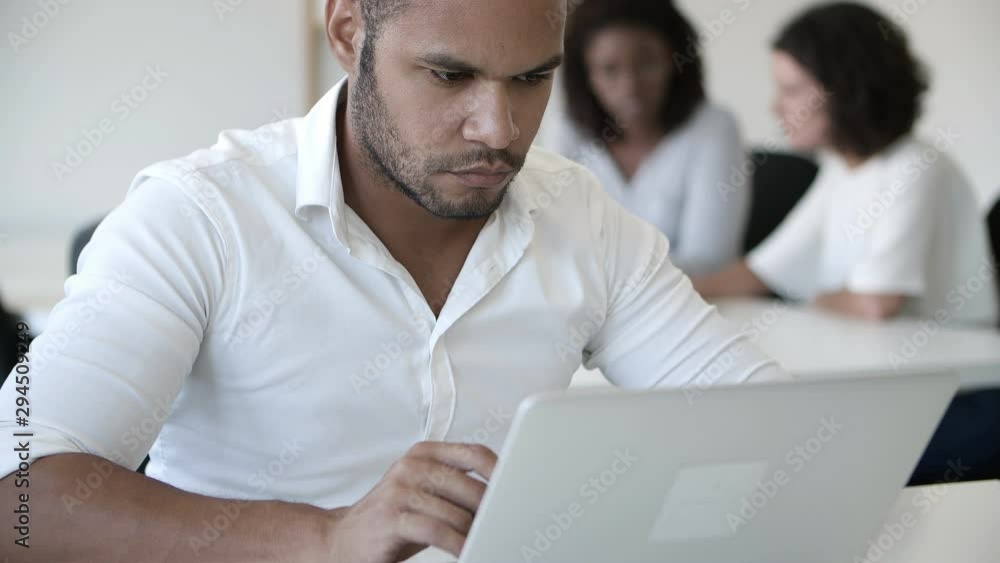 Pensive handsome man using laptop at modern office. Front view of young confident programmer working at office. Technology concept Pensive handsome man using laptop at modern office. Front view of young confident programmer working at office. Technology concept