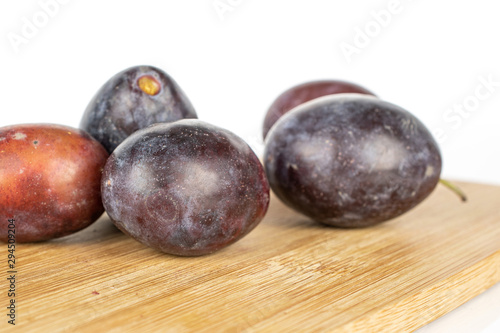 Group of five whole sweet purple plum on bamboo cutting board isolated on white background