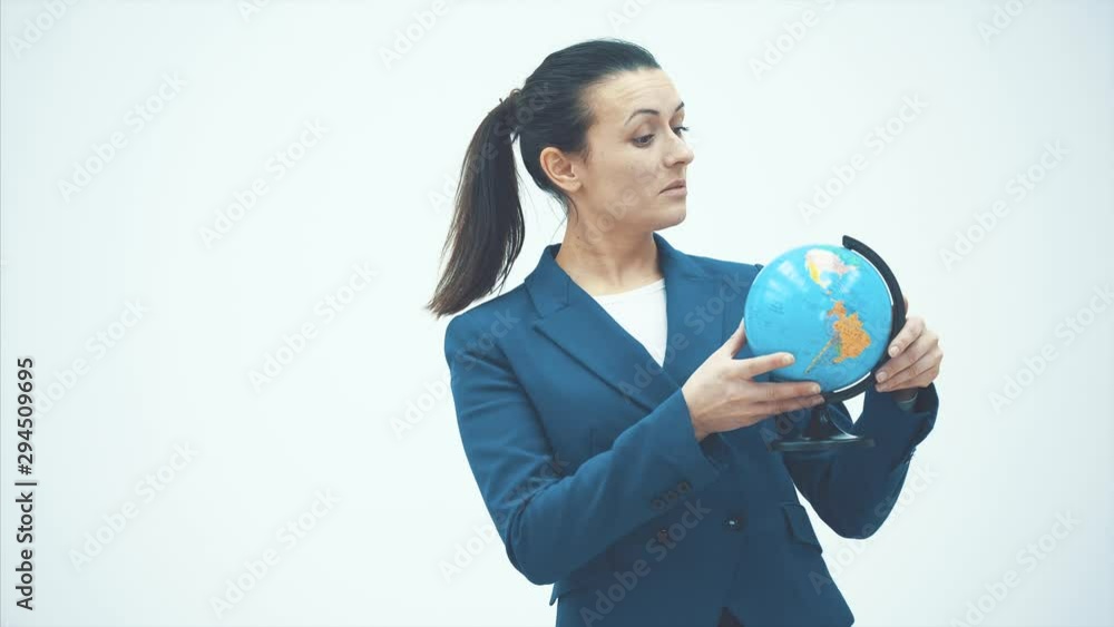 Young intelligent teacher stands on a white background. Holds the globe and watches how it spins. Surprised. Close-up Young intelligent teacher stands on a white background. Holds the globe and watches how it spins. Surprised. Close-up