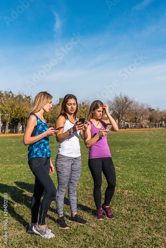 Happy friends in the park on a sunny day . Lifestyle portrait of three women friends enjoy nice day with their smartphones.