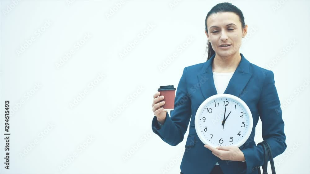Young good teacher standing on a white background. Holds a white clock and coffee. Sincerely smiles. Young good teacher standing on a white background. Holds a white clock and coffee. Sincerely smiles.