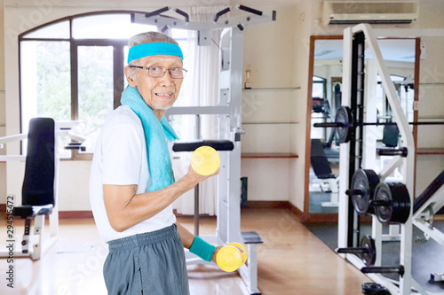 Senior man holding two dumbbells in gym center