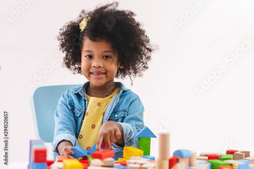 Little afro girl smiling and playing colorful wooden toys.