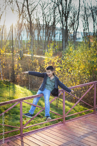 Portrait of caucasian boy in warm clothes playing and balancing on railing of the bridge in autumn park.