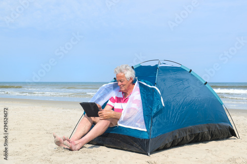 Man with digital tablet camping in shelter at the beach