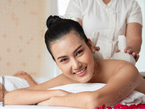 Beautiful young asian woman lying relaxing and smile on the bed having a massage with herbal compresses in a spa. Thai massage for health. Select focus face women