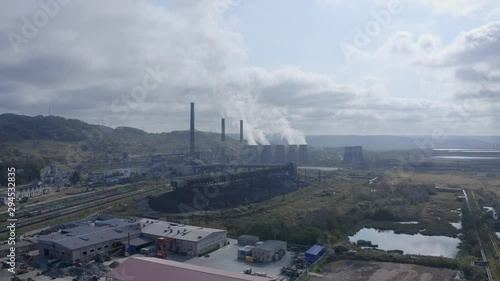 Landscape view with a coal-fired power station with its chimneys and funnels releasing white smoke into the air on a sunny and cloudy day. Aerial shot photo