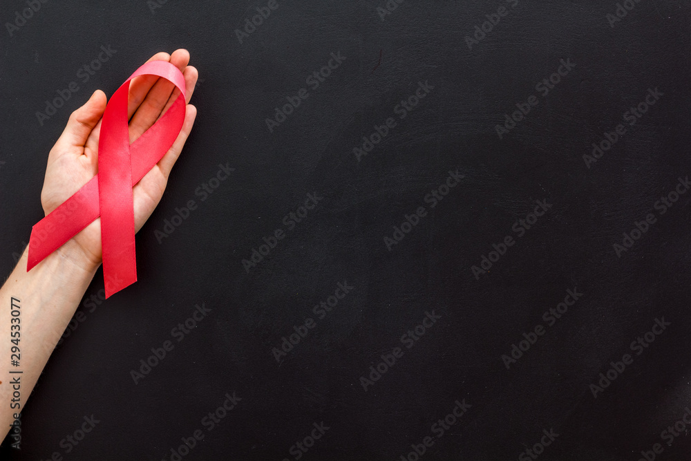 Pink ribbon in hands as symbol of breast cancer awareness on black background top view space for text