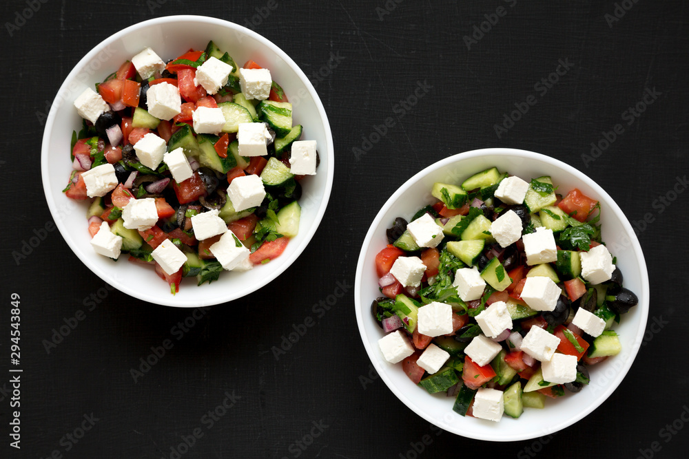 Homemade Shepards salad with cucumbers, feta and parsley in white bowls on a black backgrounds, top view. From above, overhead, flat lay. Close-up. Homemade Shepards salad with cucumbers, feta and parsley in white bowls on a black backgrounds, top view. From above, overhead, flat lay. Close-up.
