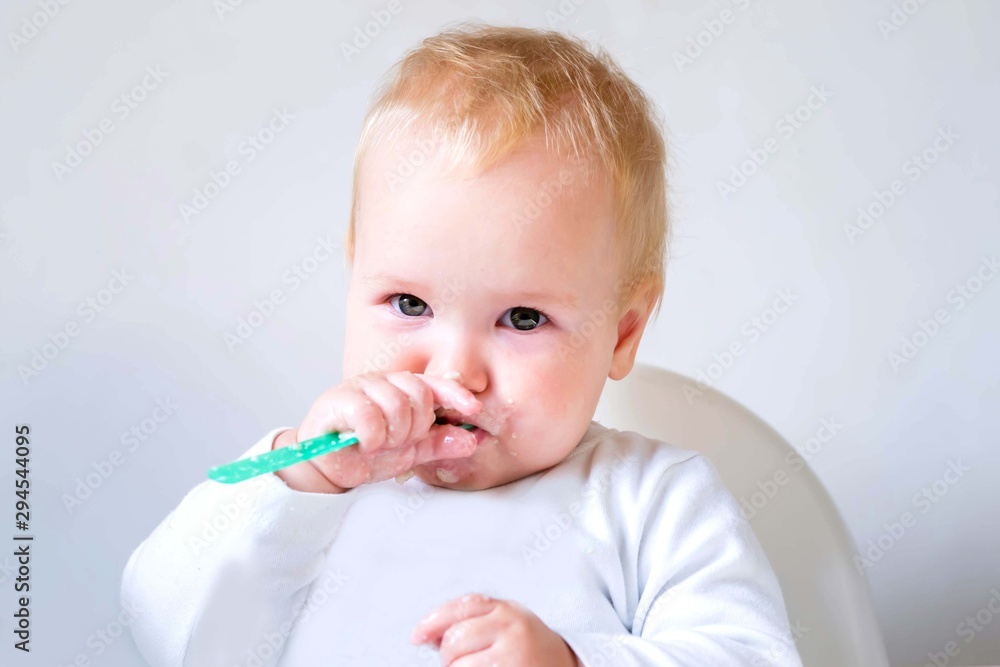 Baby, little girl eating lunch with green plastic spoon. Delicious food. Baby eating with pleasure. White plastic chair for feeding. Baby, little girl eating lunch with green plastic spoon. Delicious food. Baby eating with pleasure. White plastic chair for feeding.