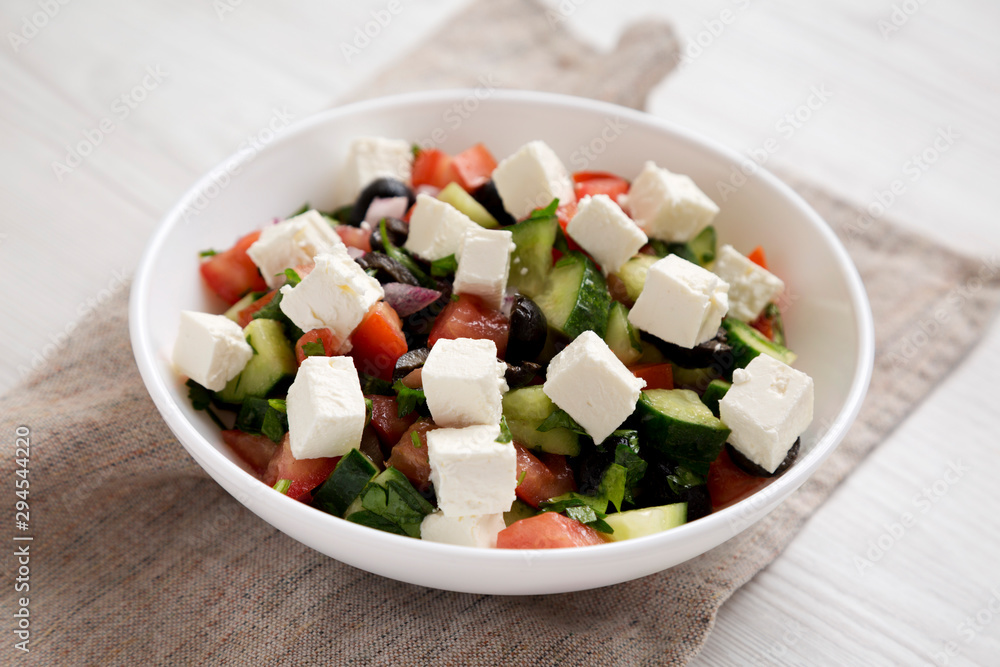 Homemade Shepherds salad with cucumbers, parsley and feta in a white bowl on a white wooden surface, side view. Close-up. Homemade Shepherds salad with cucumbers, parsley and feta in a white bowl on a white wooden surface, side view. Close-up.