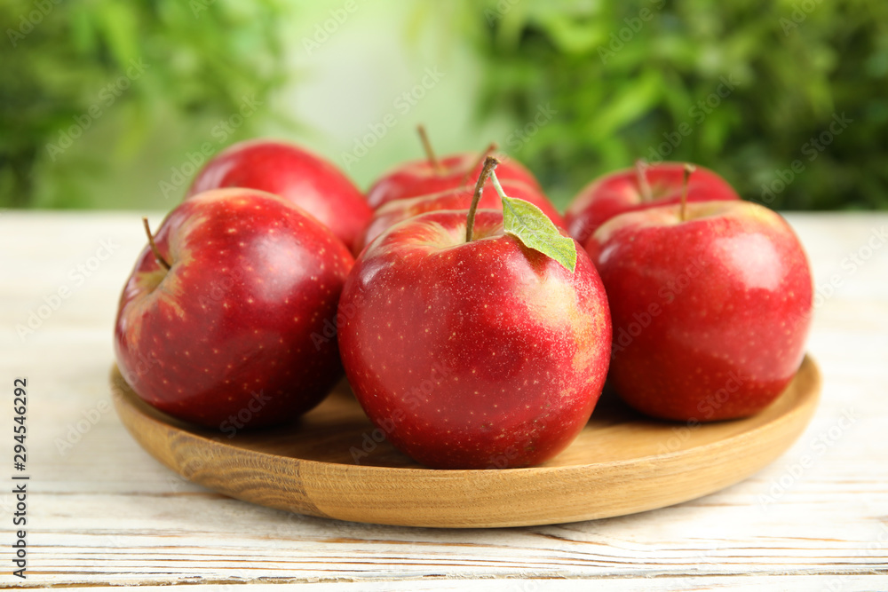 Wooden plate with ripe juicy red apples on white table against blurred background Wooden plate with ripe juicy red apples on white table against blurred background