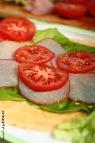 Making wrap tortilla sandwich with ham, tomato, lettuce.