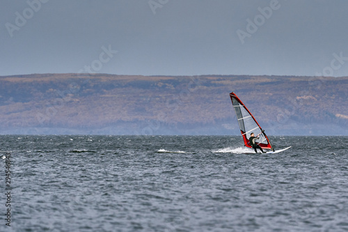 A male athlete is interested in windsurfing. He moves on a Sailboard on a large lake on an autumn day. © afefelov68