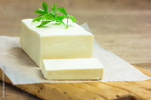 Cuadro en lienzo A few slices of yellow butter cut off from a just opened pack of butter with a knife on a brown wooden cutting board
