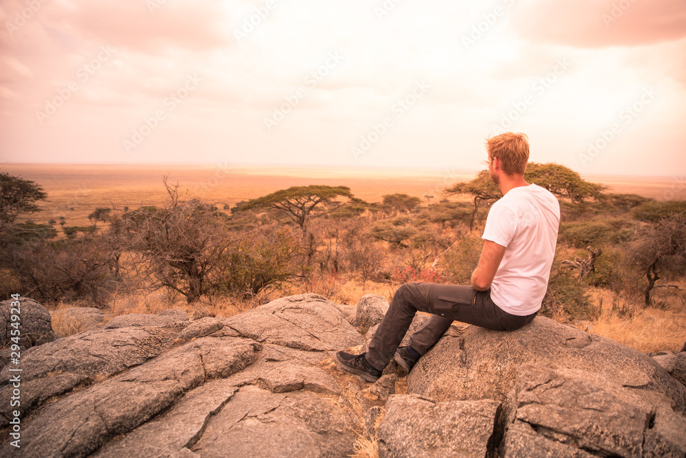 Man at view point looking to the bush savannah of Serengeti at sunset, Tanzania - Safari in Africa