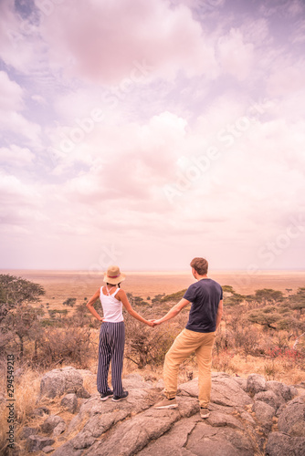 Young couple at view point looking to the bush savannah of Serengeti at sunset, Tanzania - Safari in Africa