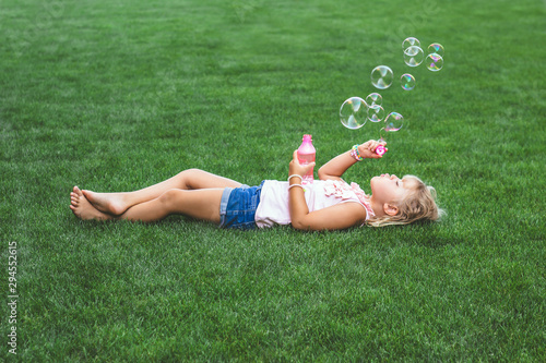 Little girl laying on the grass, blowing soap bubbles
