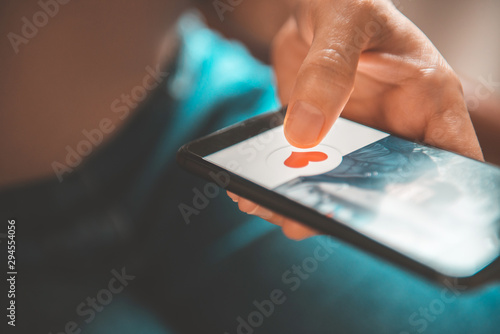 Finger of woman pushing heart icon on screen in mobile smartphone application. Online dating app, valentine's day concept.