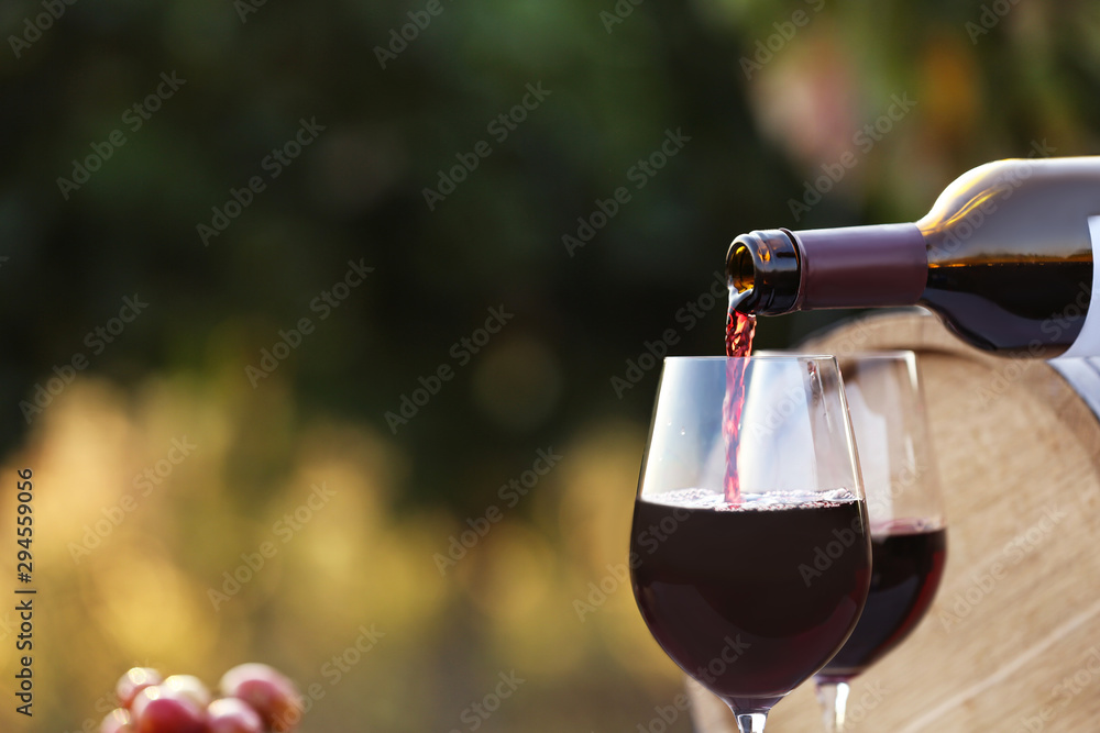 Pouring wine from bottle into glass outdoors, closeup