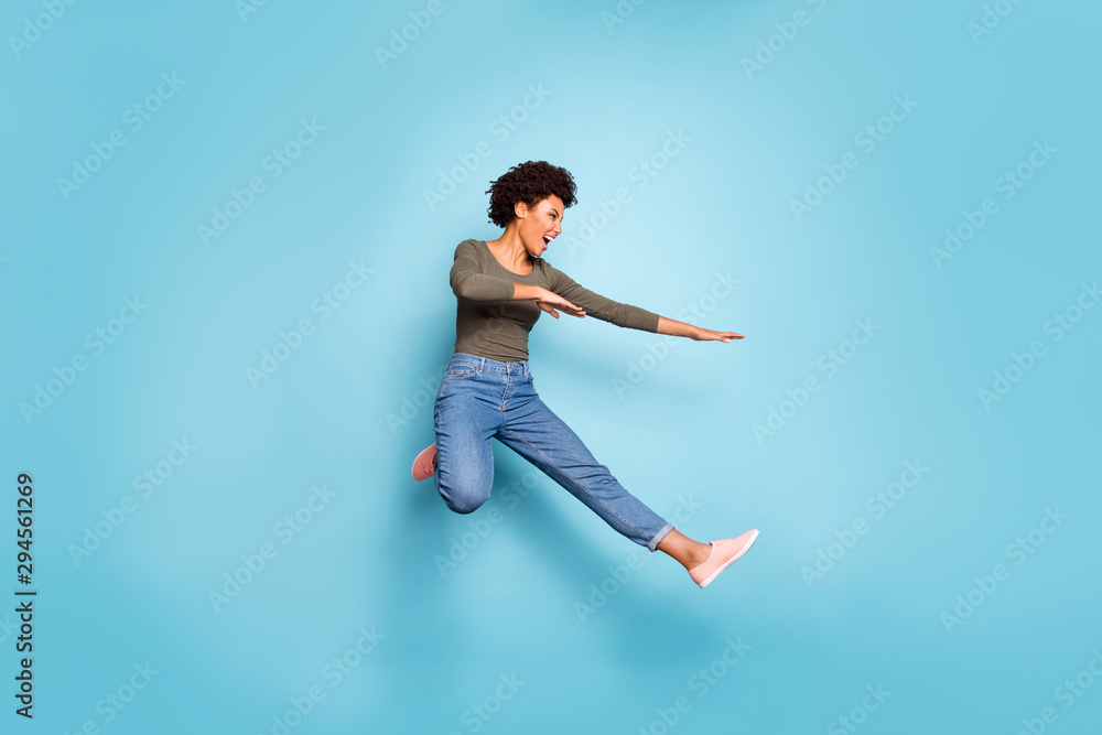 Full length photo of dark skin pretty wavy lady jumping high dancing modern youngster moves wear casual outfit isolated pastel blue color background