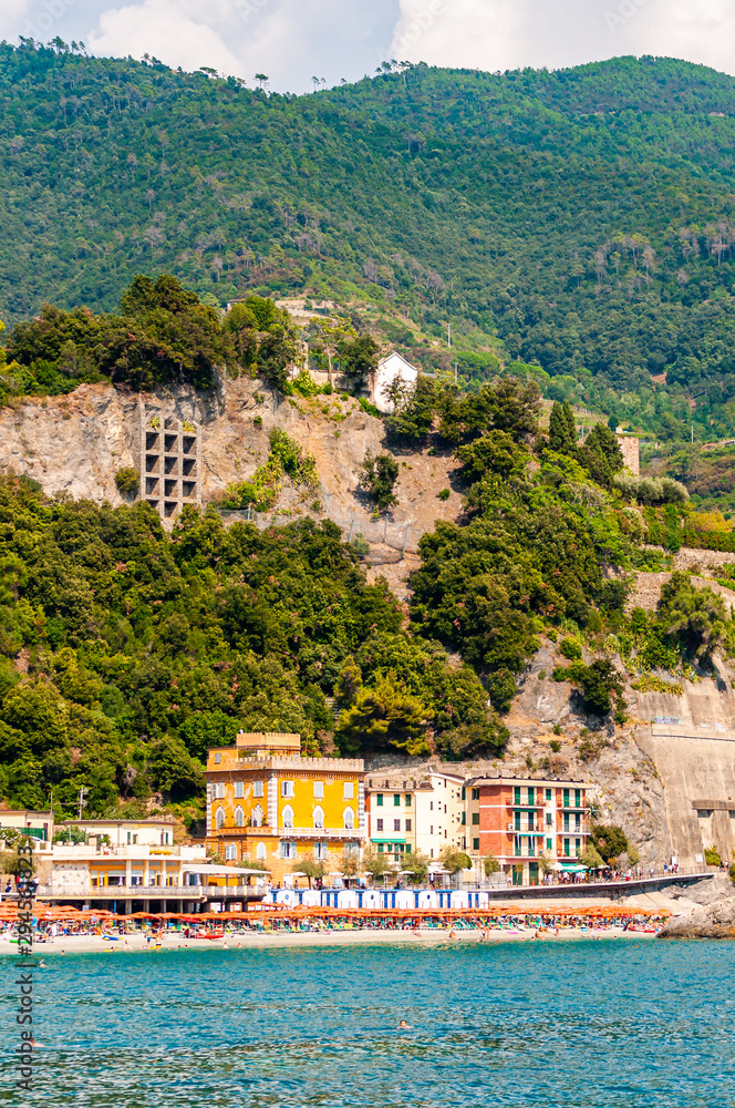 Transparent, clear water of Ligurian Sea, the beach full of people, colorful waterfront buildings and high green mountains on the background in Monterosso Al Mare, Cinque Terre