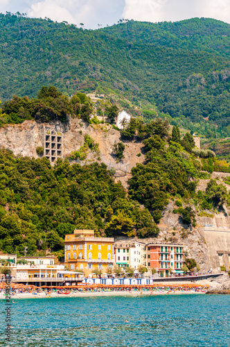 Transparent, clear water of Ligurian Sea, the beach full of people, colorful waterfront buildings and high green mountains on the background in Monterosso Al Mare, Cinque Terre