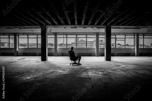 Man sitting in front of a large window in an empty hall of an abandoned building - black and white