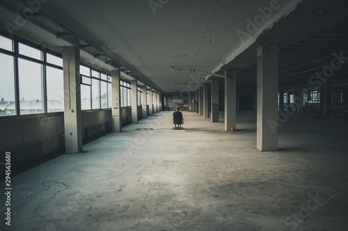 Man sitting in front of a large window in an empty hall of an abandoned building