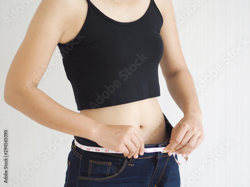 weight loss and slim body in asian woman with wrapped around her waistband by tape measure use for workout,fitness or diet and burn,block or detox and dietary supplement product on white background.