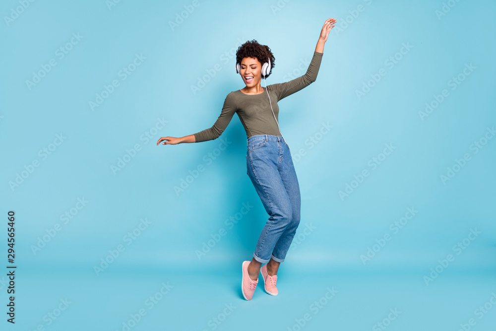 Full body photo of cheerful funny girl have free time listen music on her headset dance sing enjoy wear stylish green pullover denim jeans sneakers isolated over blue color background Full body photo of cheerful funny girl have free time listen music on her headset dance sing enjoy wear stylish green pullover denim jeans sneakers isolated over blue color background